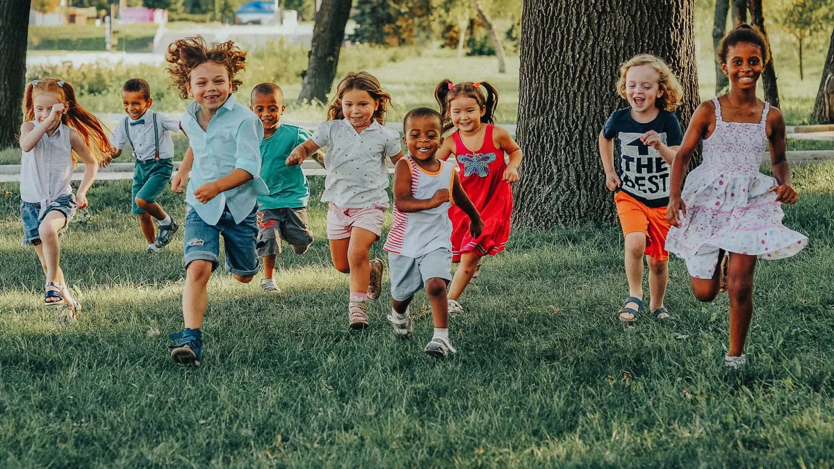 a group of preschoolers running on the grass in the Park
