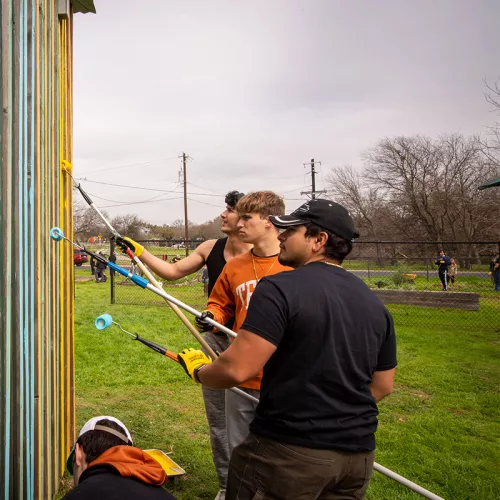 Teens use paint rollers to paint an outdoor shed
