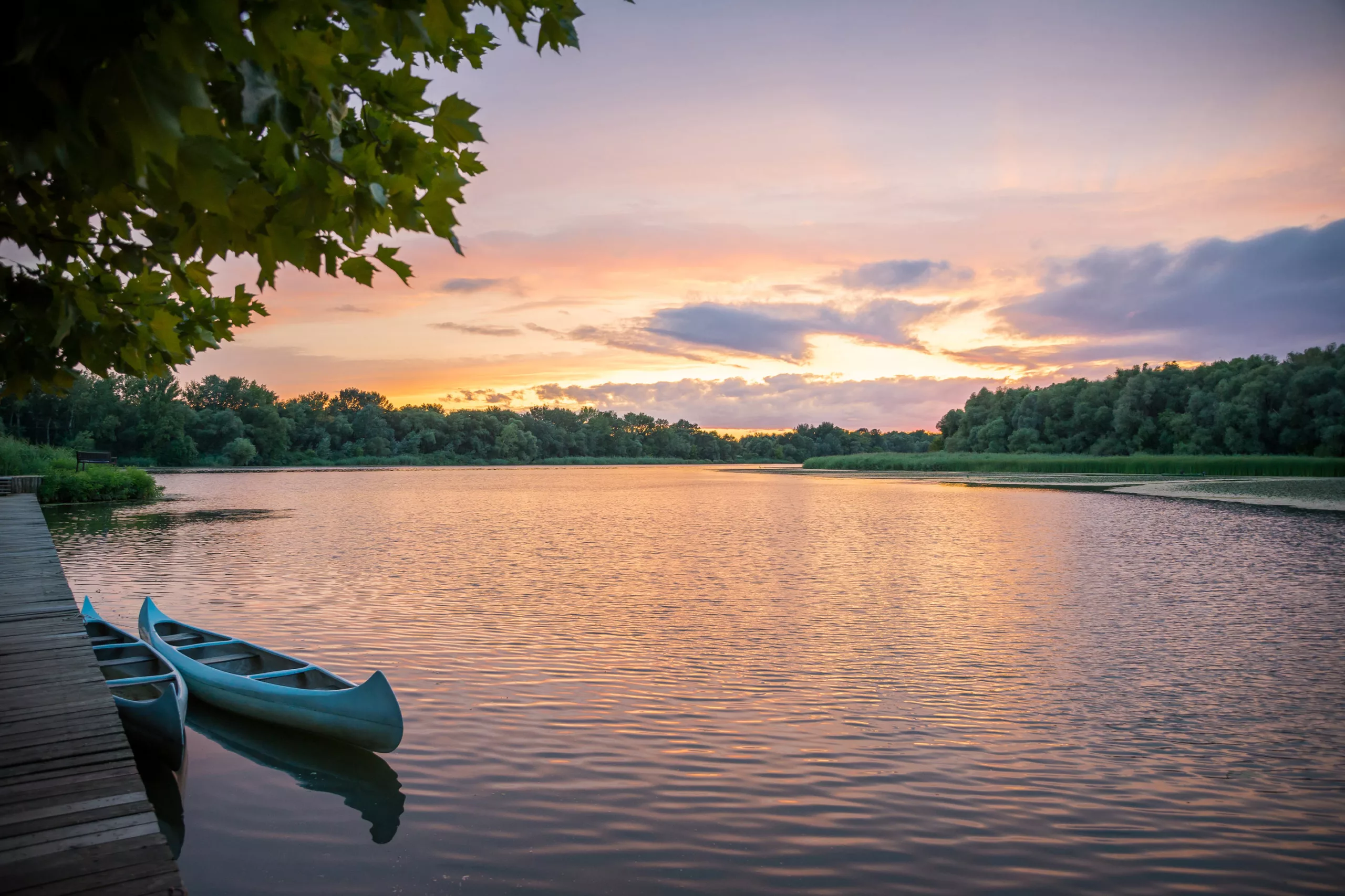A canoe rests against a wooden dock on a placid water during a twilight moment.
