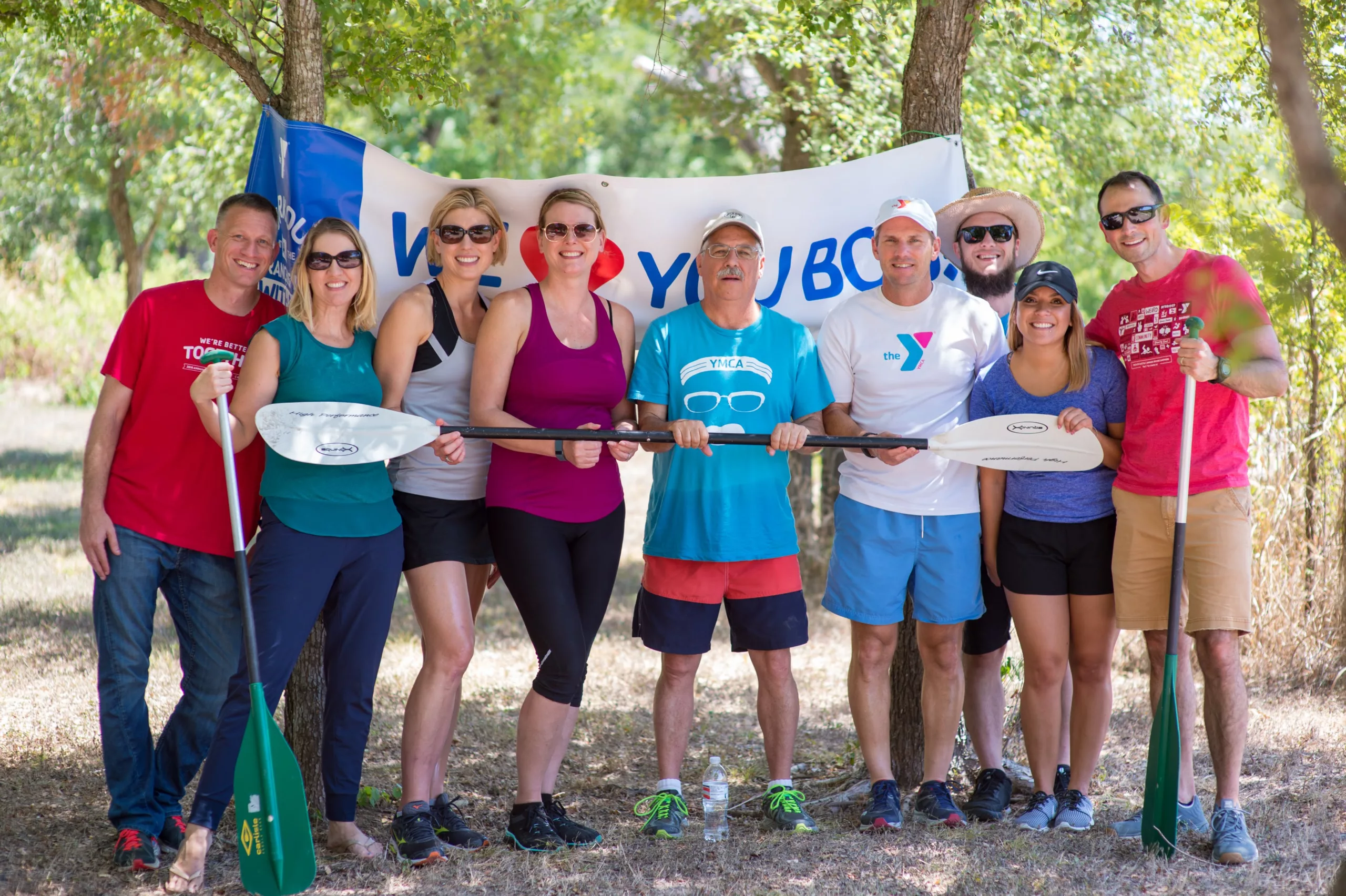 A group of people stand outdoors wearing exercise clothes. They are holding an oar.