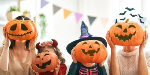 A family holds up carved pumpkins in front of their faces.