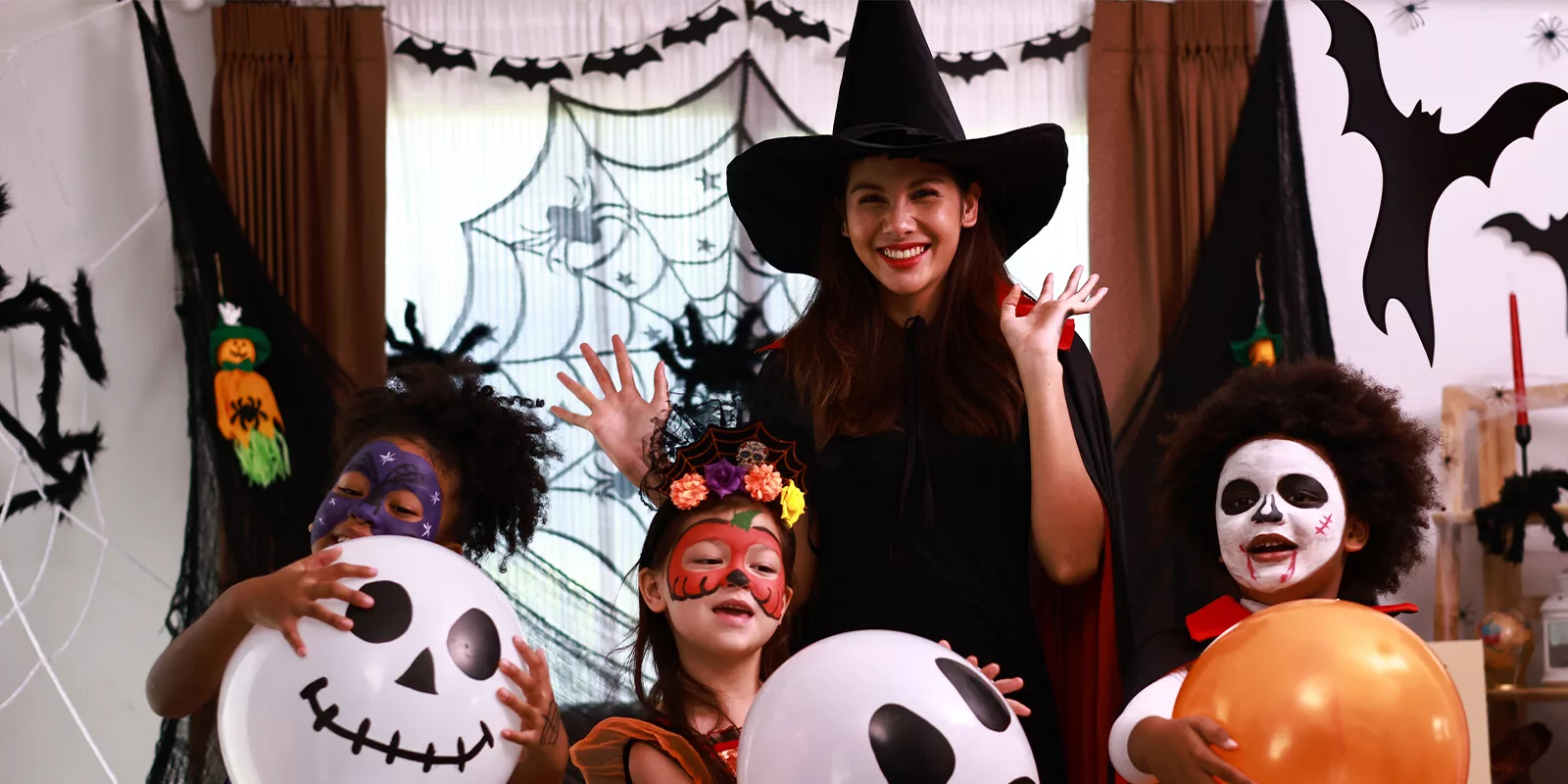 A group of children dressed in halloween costumes hug spooky balloons