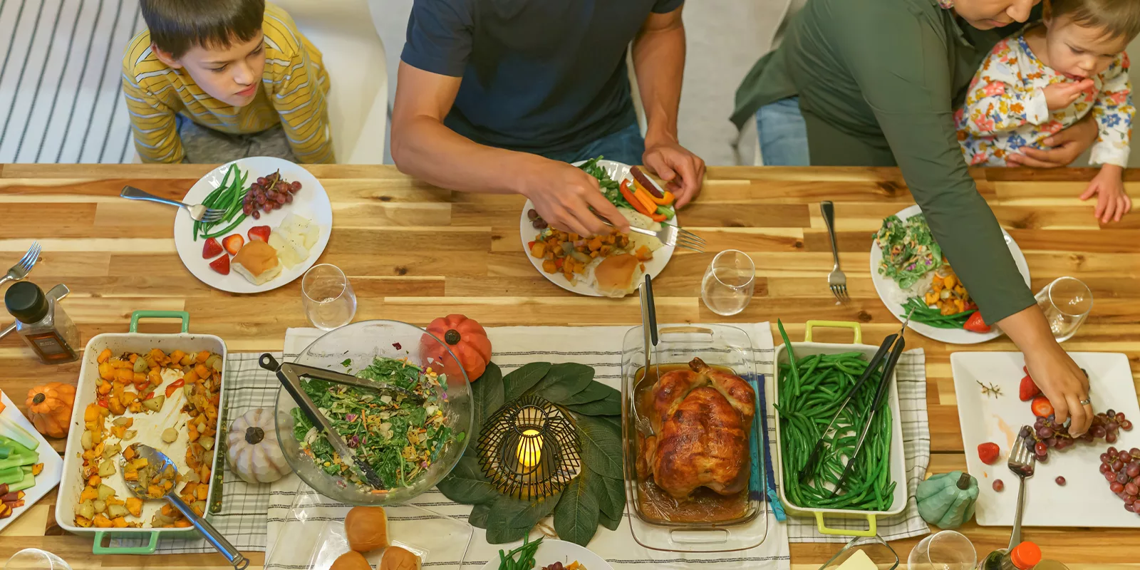 A table set with holiday food is seen from above. Family members fill their plates.
