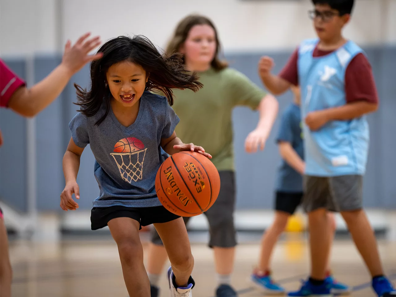 Children play a casual game of basketball in a gymnasium.