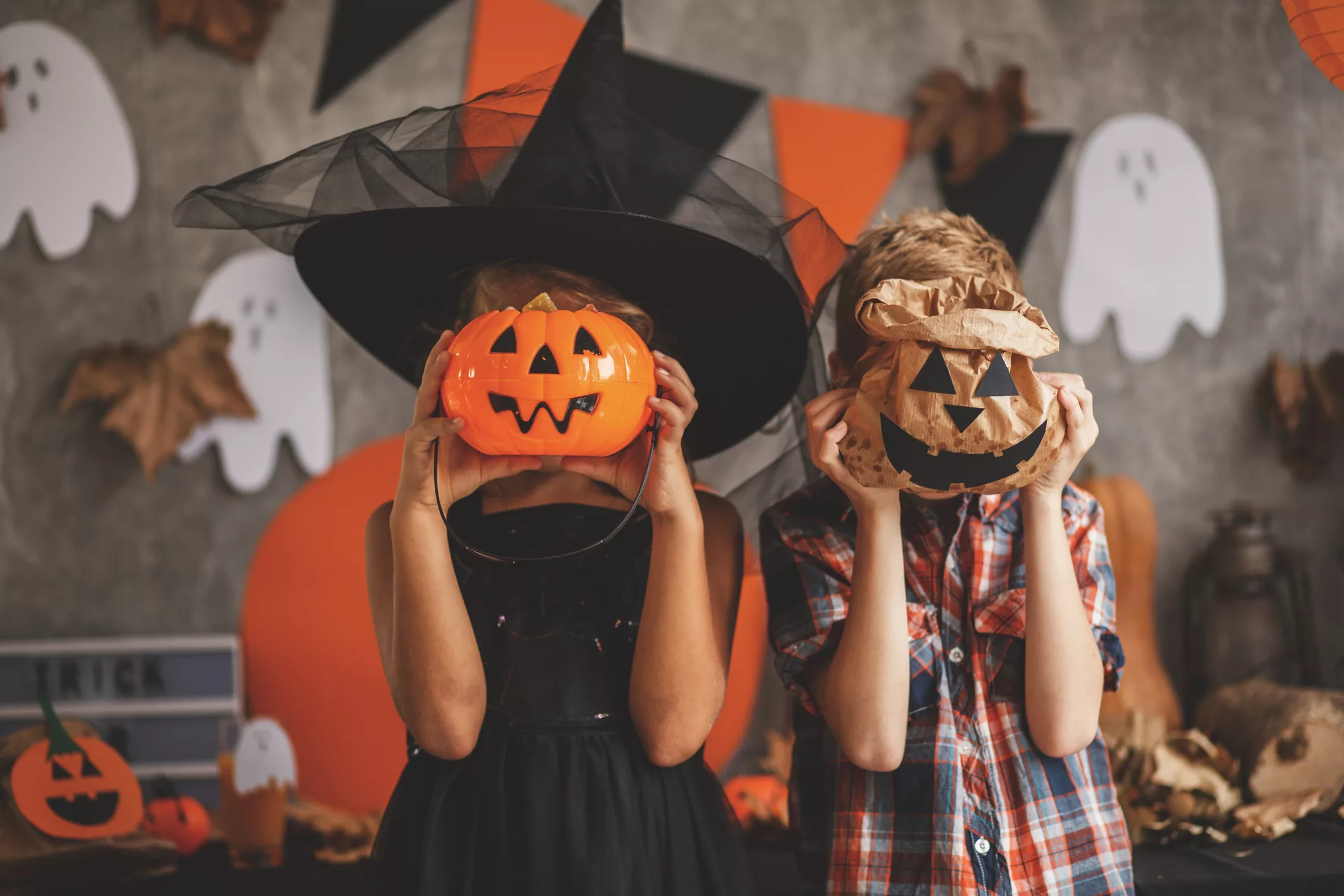 Children playing with Halloween decoration two children in costumes holding jack-o-lanterns in front of their faces.