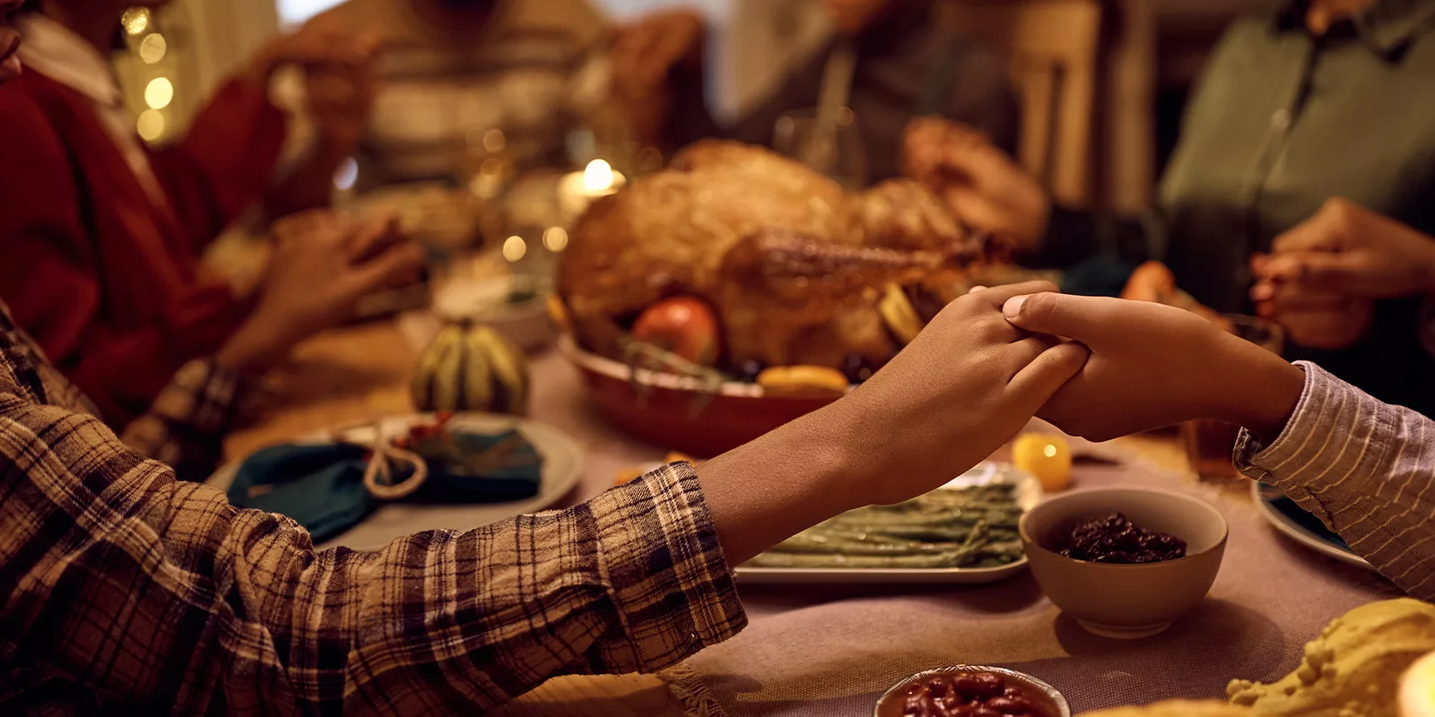 Hands are seen holding one another before a table laid with food.