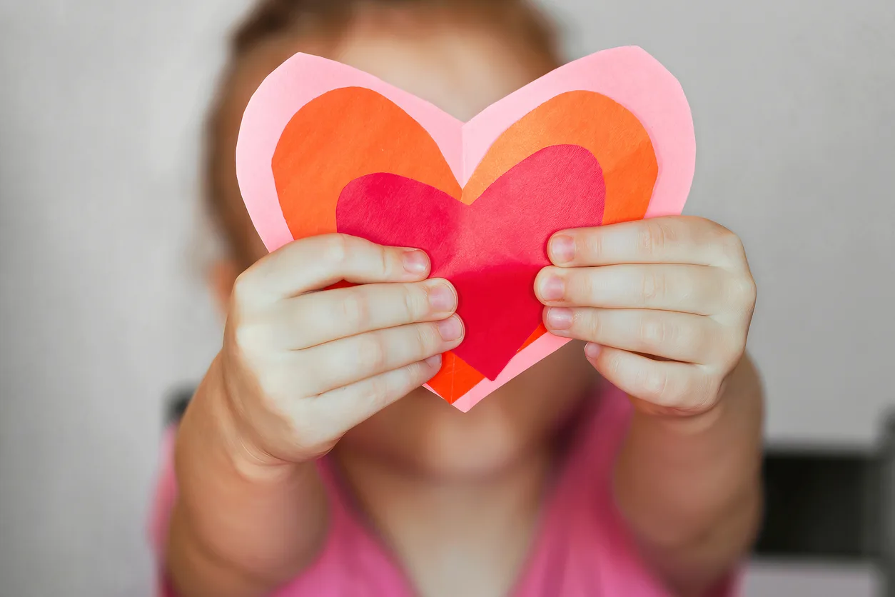 DIY holiday card with a red paper heart, a symbol of love. child holding