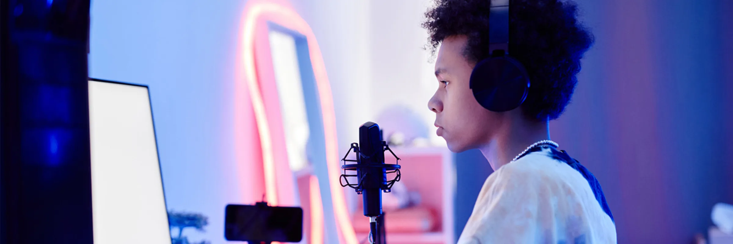 A teen sits in a recording booth with lots of tech around.