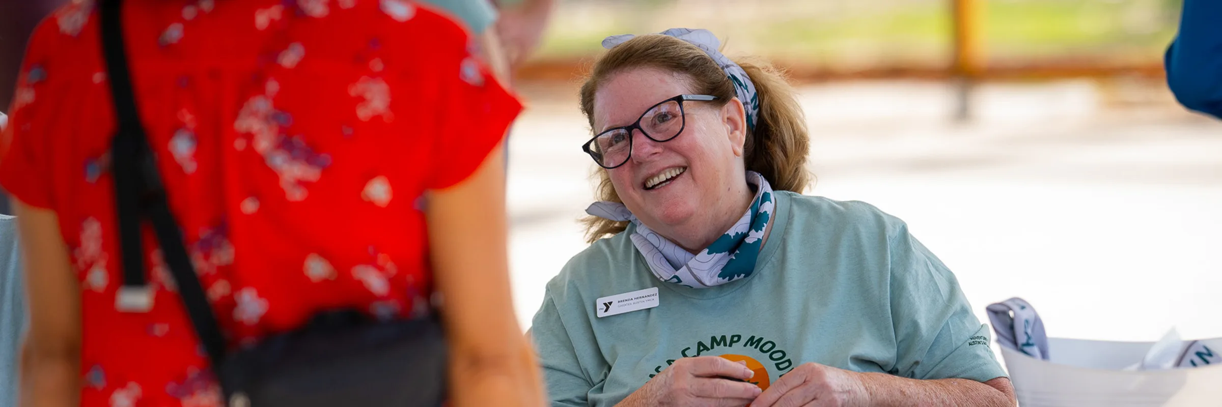 A woman smiles while sitting at an outdoor table.