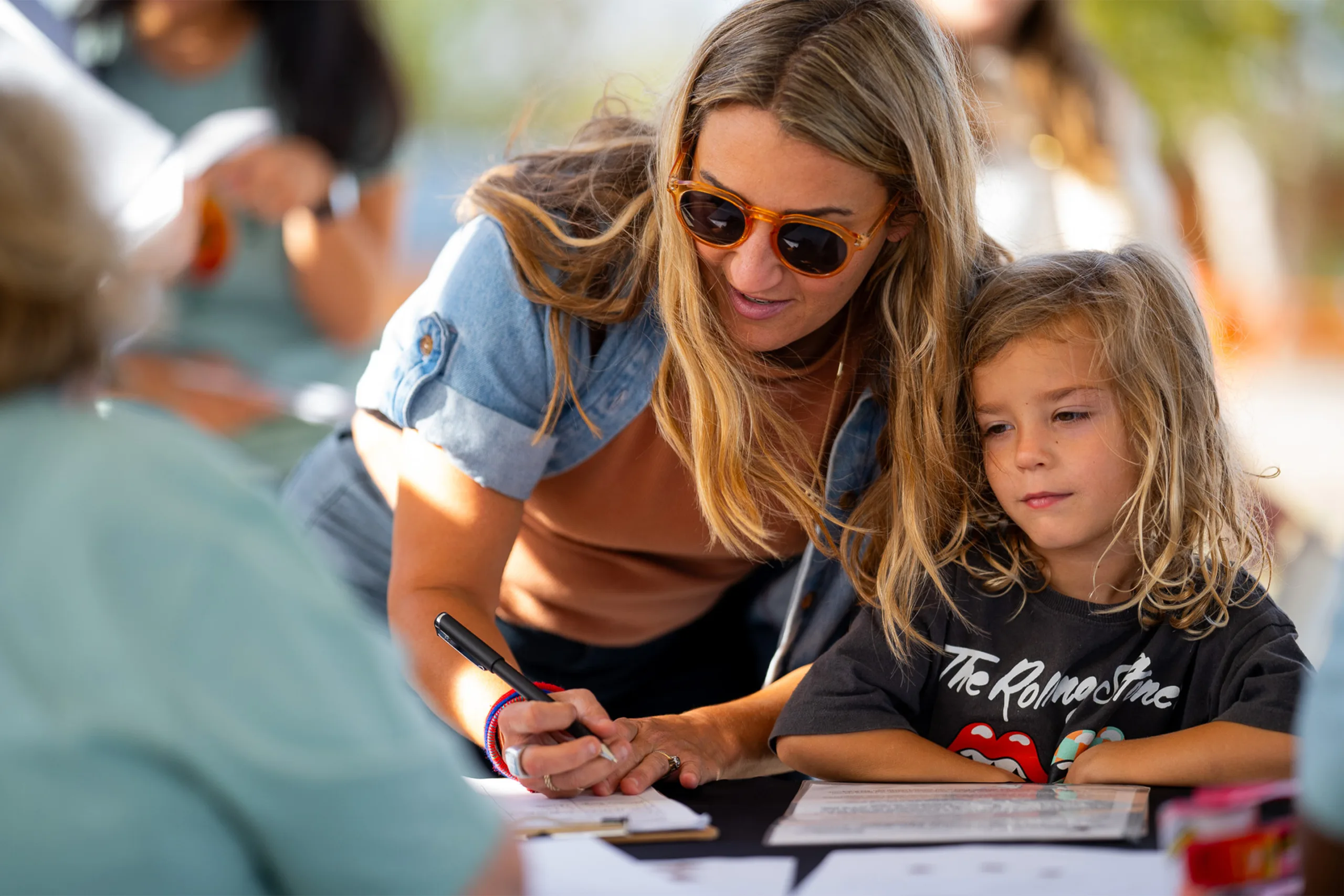 A woman writes using a clipboard while a child looks on.