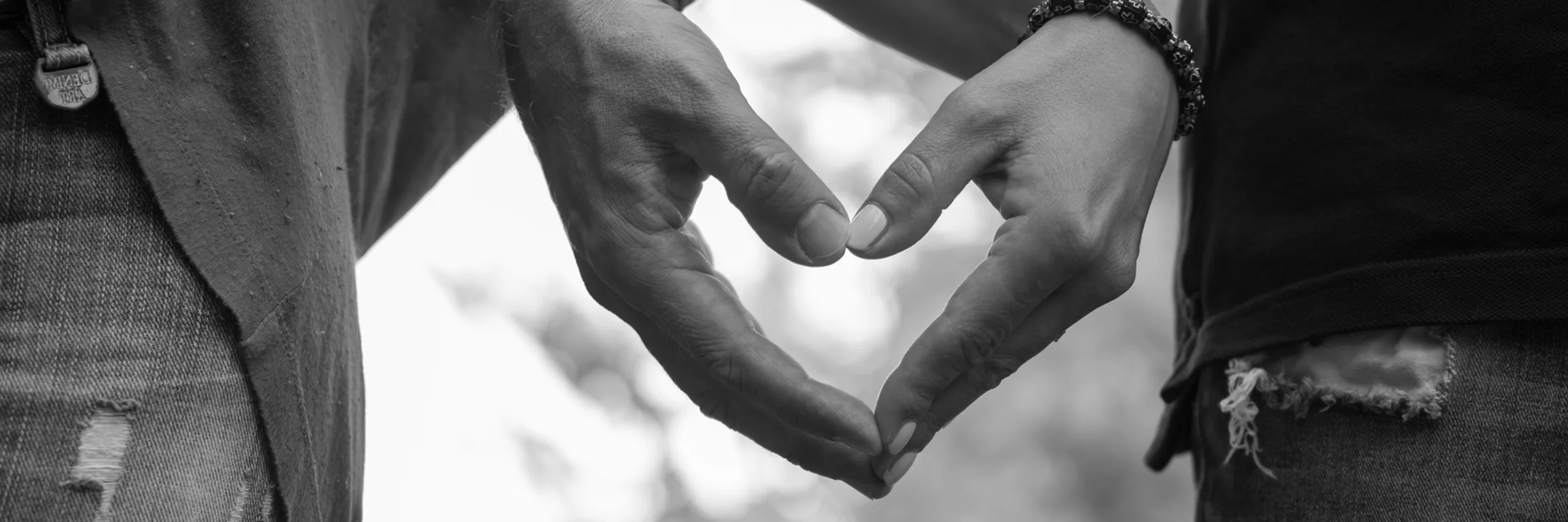 A couple standing next to one another form a heart shape with their hands