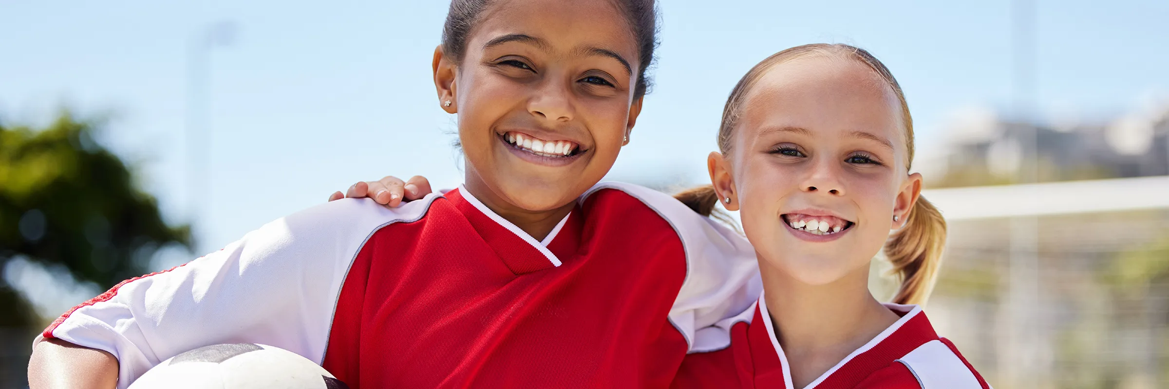 Two children wearing team uniforms stand together smiling
