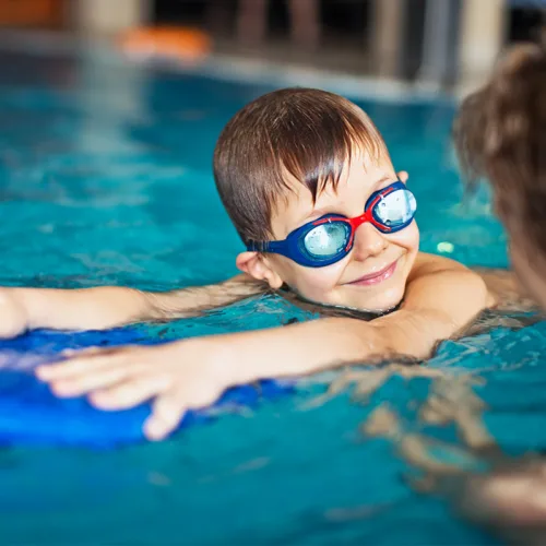 preschool-swim-lesson-square A young child wearing goggles participates in a swimming lesson in an indoor pool.