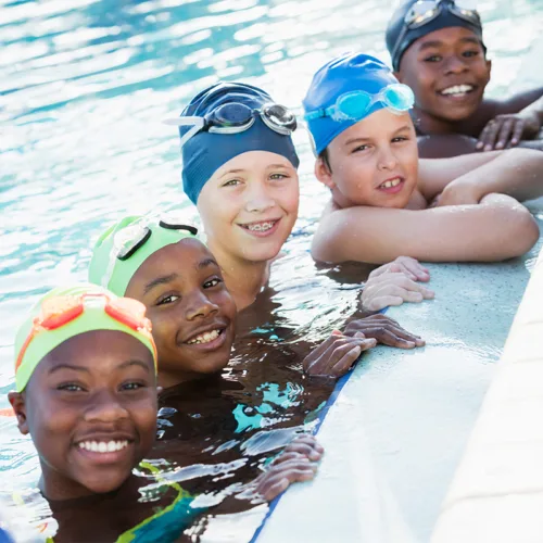 swim-team-square Children wearing colorful swim caps pose at the edge of a pool.