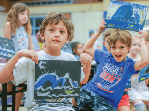 Children at camp show off their art projects where they made waves with chalk on black paper.