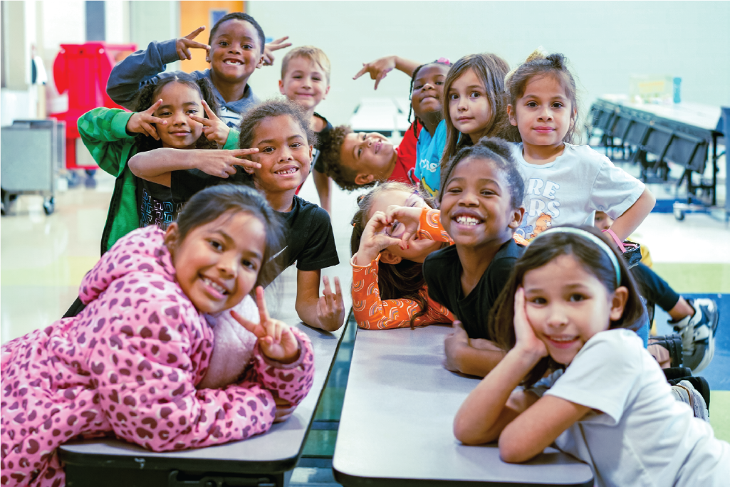 A diverse group of children in a school cafeteria smile for the camera