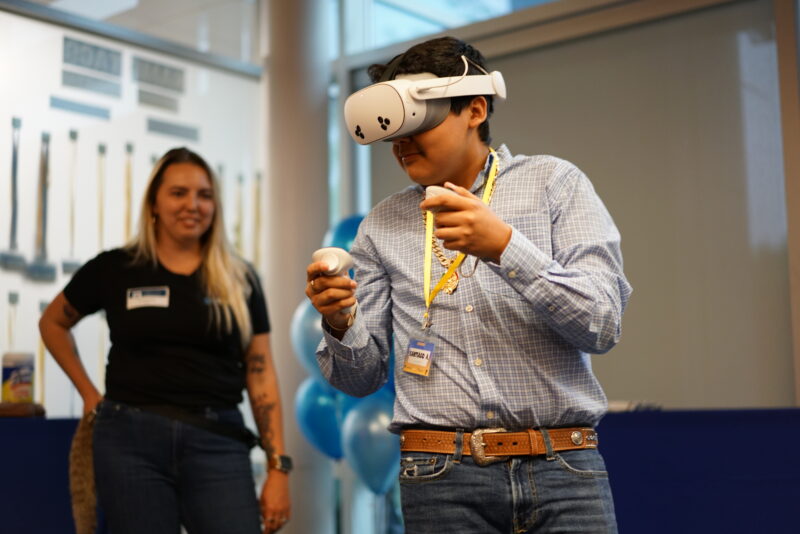 DSC04996 teen using VR headset with mentor smiling in background