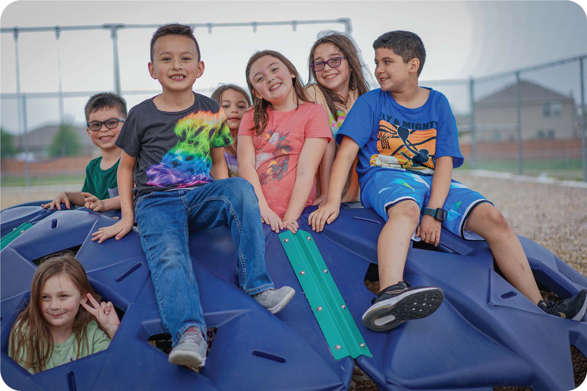 A group of children sit together on top of a playground structure while smiling