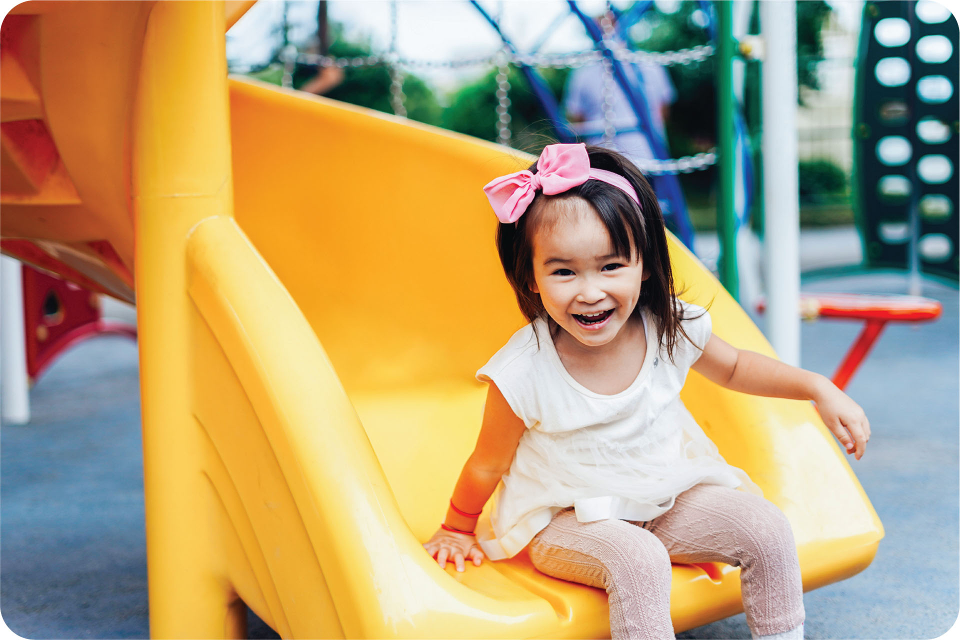 A girl who just slide down a yellow slide smiles at the camera