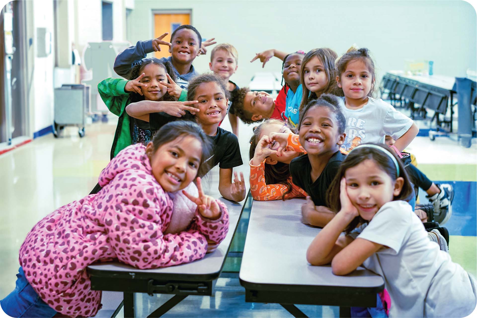 A group of children sit smiling at the camera in their school cafeteria