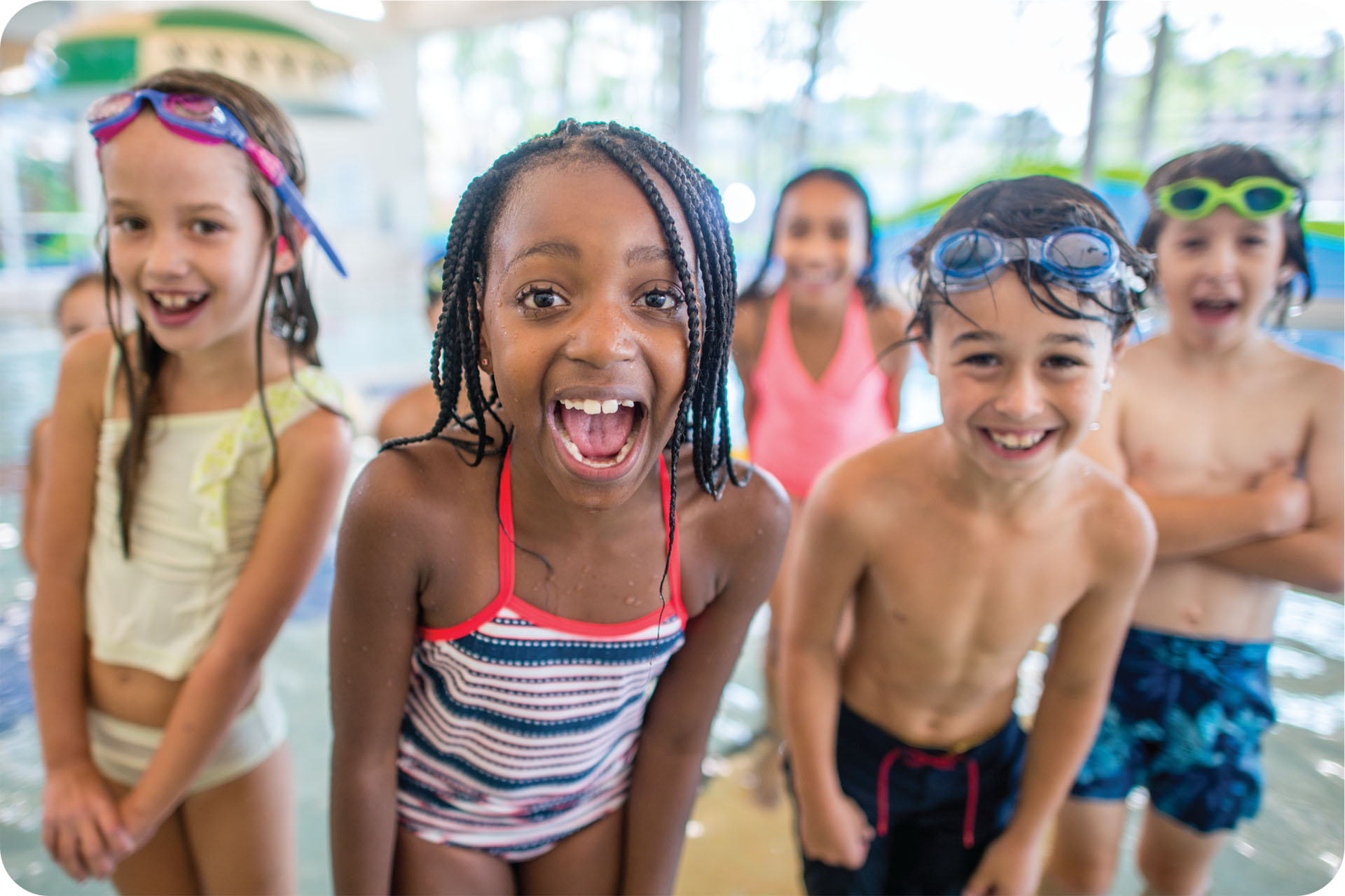 A group of five children stand in front of a pool excitedly
