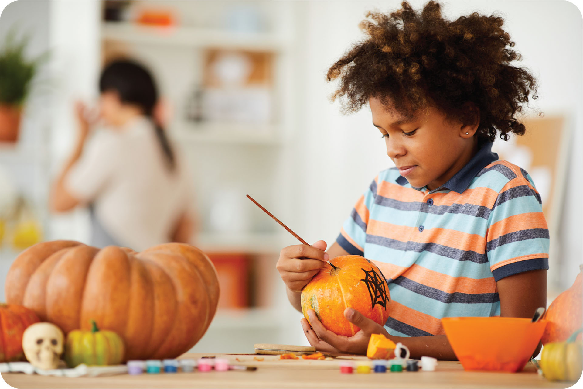 A boy holding a pumpkin paints a spider web on it