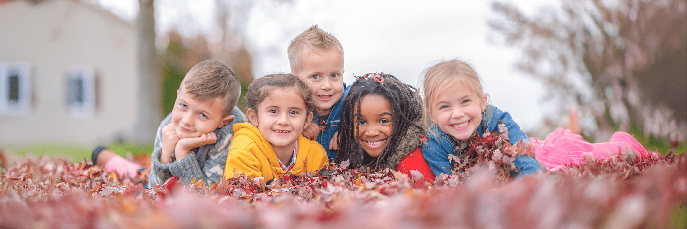 A group of 5 children smile while playing in fall leaves
