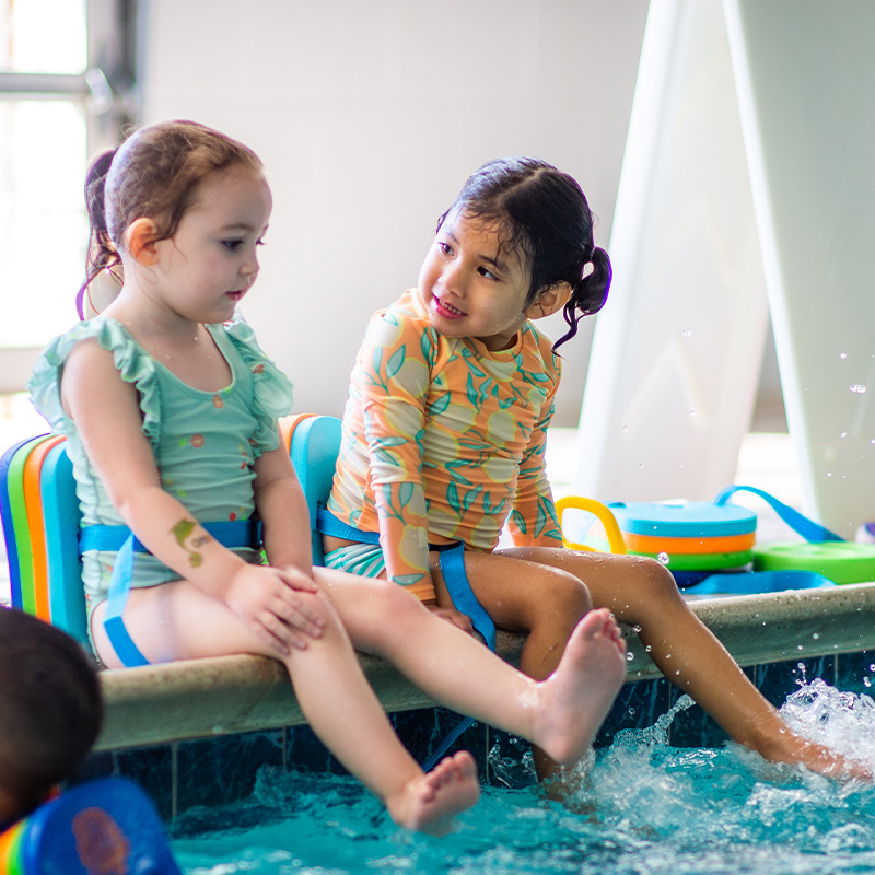 Toddlers sit at the edge of a pool for swim lessons.