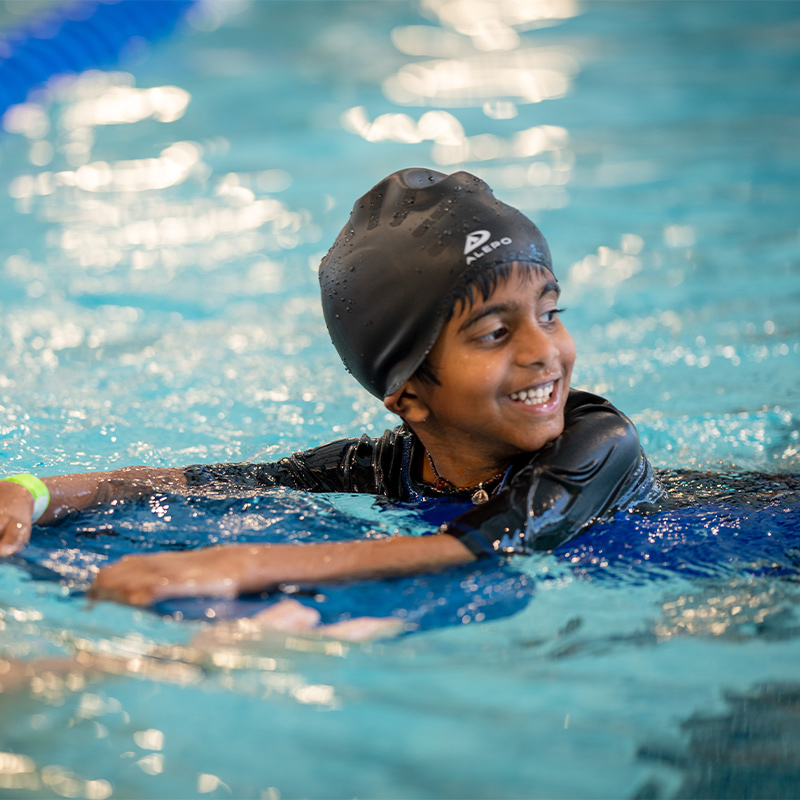 A child smiles in a swimming pool while learning stroke development in a swimming class.