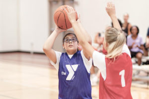 A middle school aged girl shoots a basketball while a girl on the opposite team tries to block her