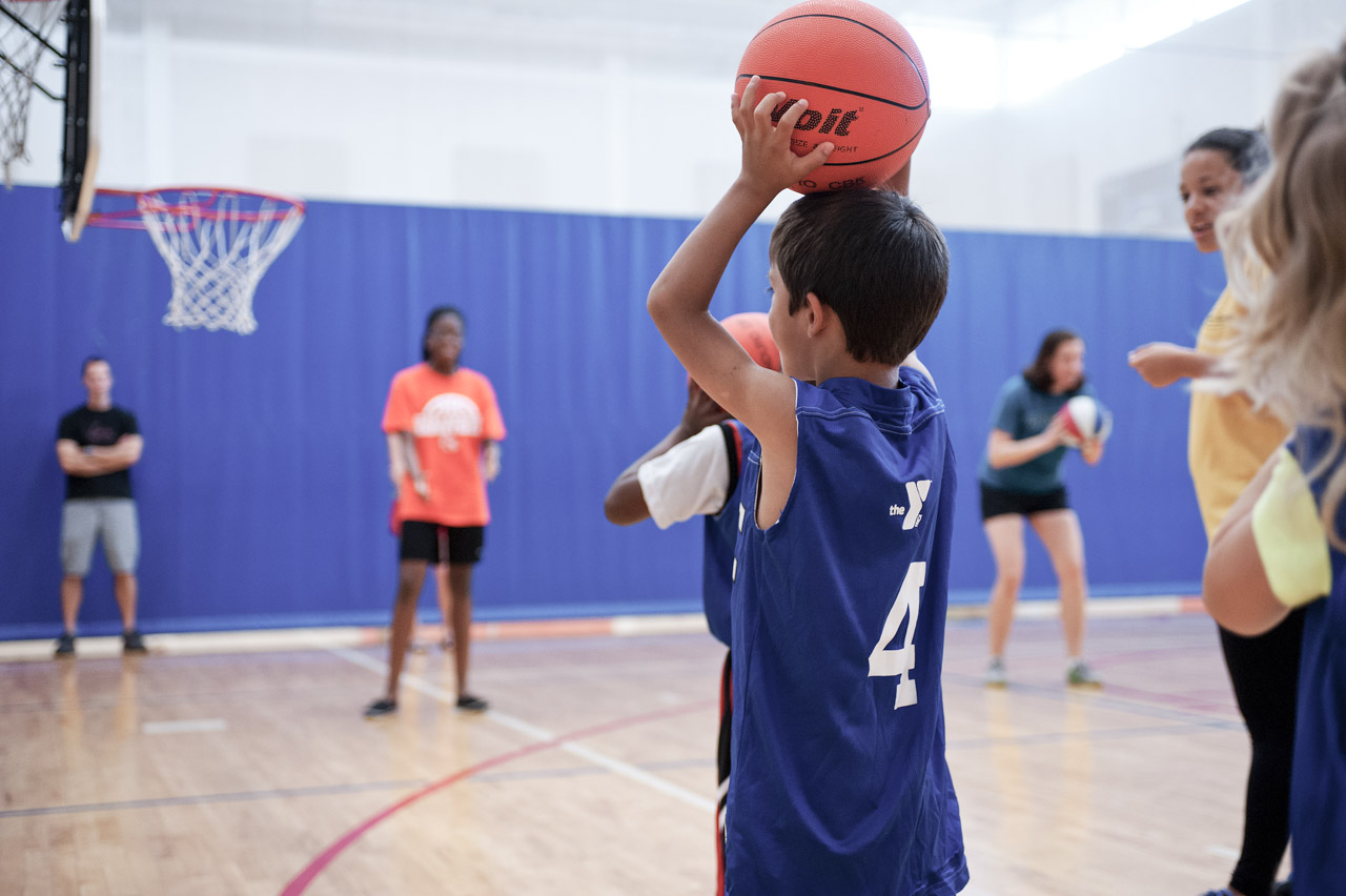 A young child playing basketball in a ymca jersey