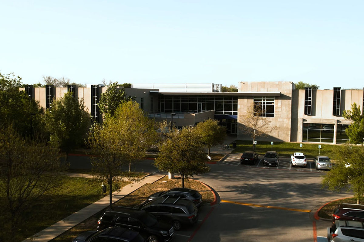 A two-story building with concrete facade. Vertical windows are on the both sides of the building with the entrance centered in the middle.