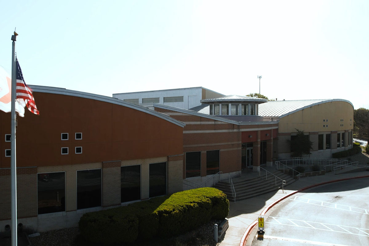A brick building with windows is viewed from an angled birds-eye view next to the flagpoles that sit out front.