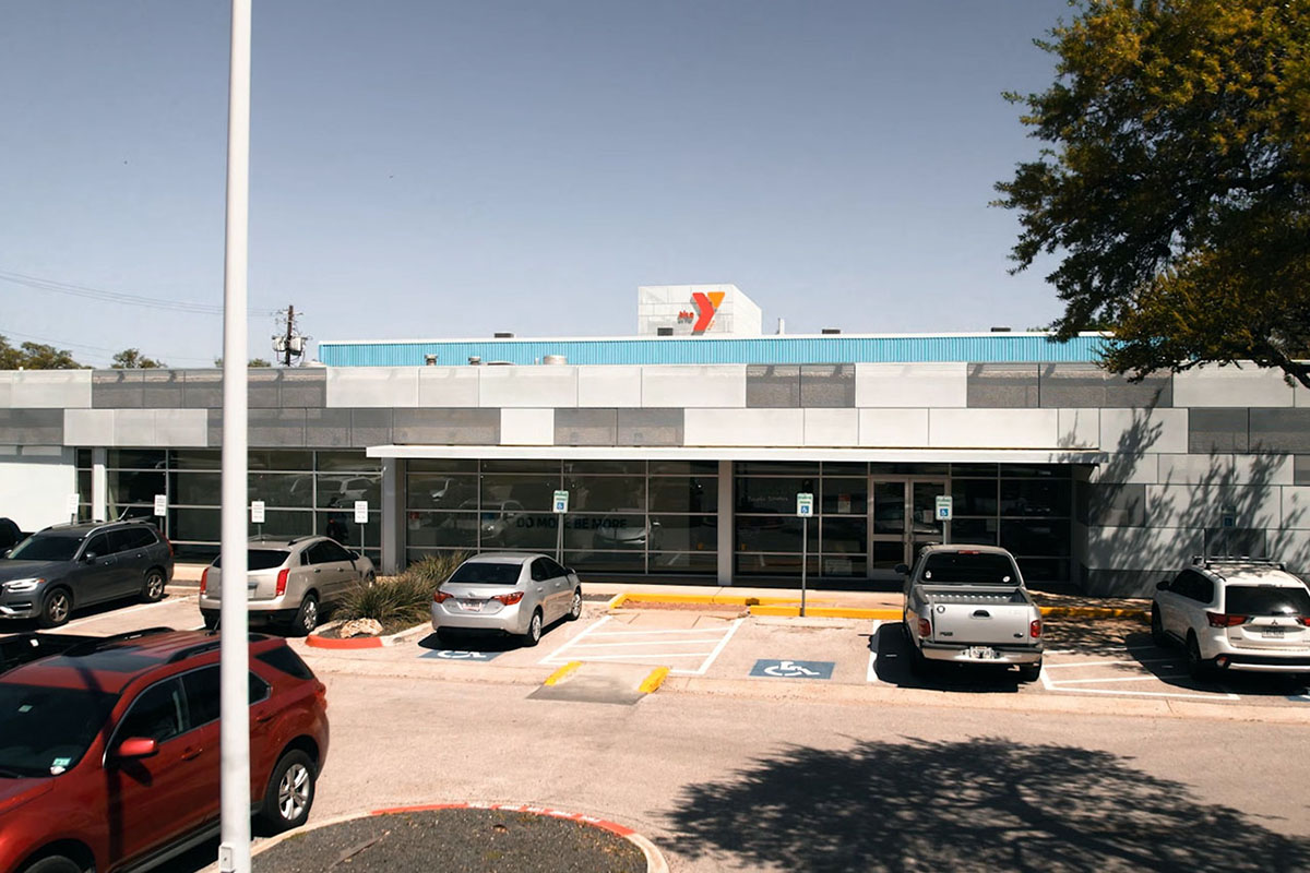 A two-story building with concrete facade. Windows line the front bottom story of the building with the entrance centered in the middle. Red and orange Y logo sits on top of building. Parking lot sits in front.