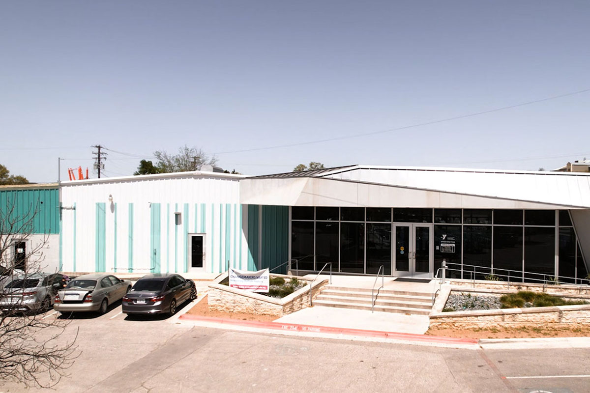 A modern-designed building with an all-window front entry and blue and white striped exterior on the sides. Parking lot sits in front. 