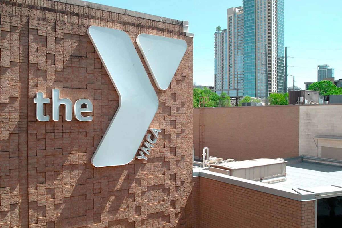 A brick building featuring a prominent white Y logo sits in foreground with part of Austin skyline in background.