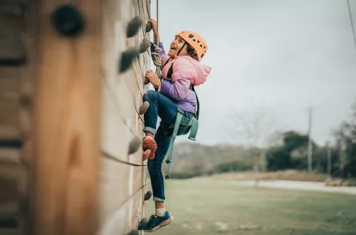 A girl climbs a rock well in rock climbing gear, looking up.