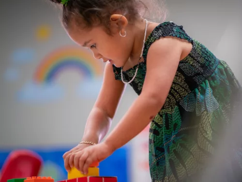 A toddler bends to work on stacking colorful blocks.