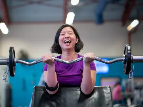 A woman flexes her arms to lift weights at a bicep curl machine.