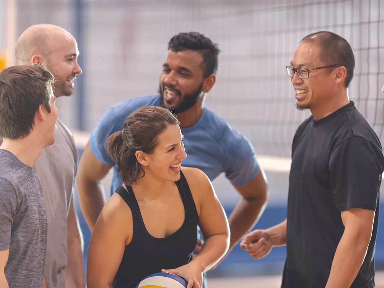 A coed group of adults pauses for laughter during a volleyball game.