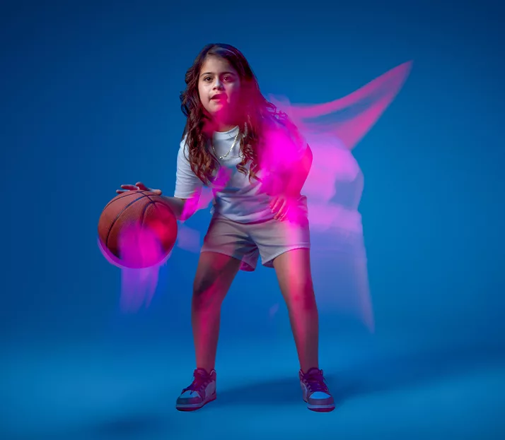 A child with long wavy hair dribbles a basketball
