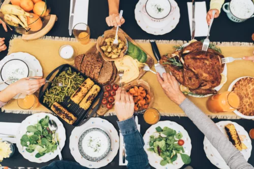Hands reach for food at over a thanksgiving holiday tablescape.