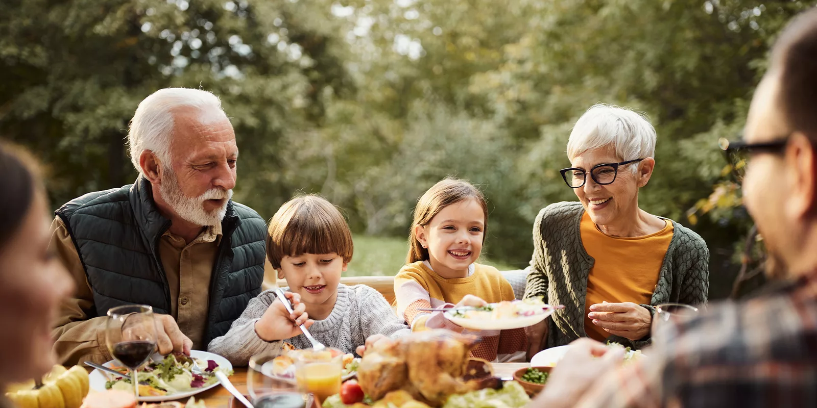A family sits before a table laid with a feast. They are outdoors.