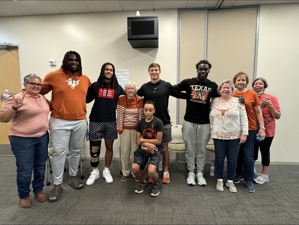 A group of people stand shoulder to shoulder wearing University of Texas gear.