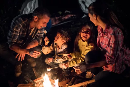 Happy family outdoors sitting by a bonfire eating marshmallows