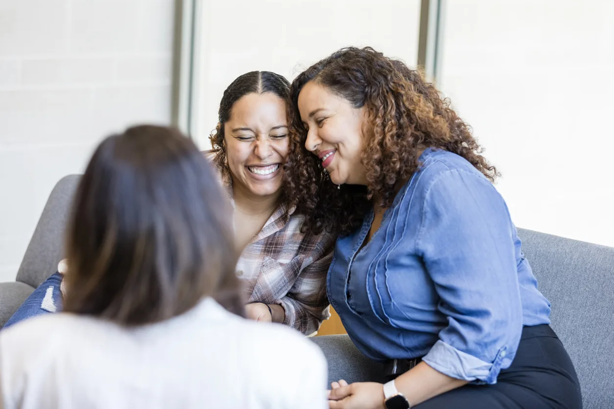 Two women smile and embrace while speaking to a counselor