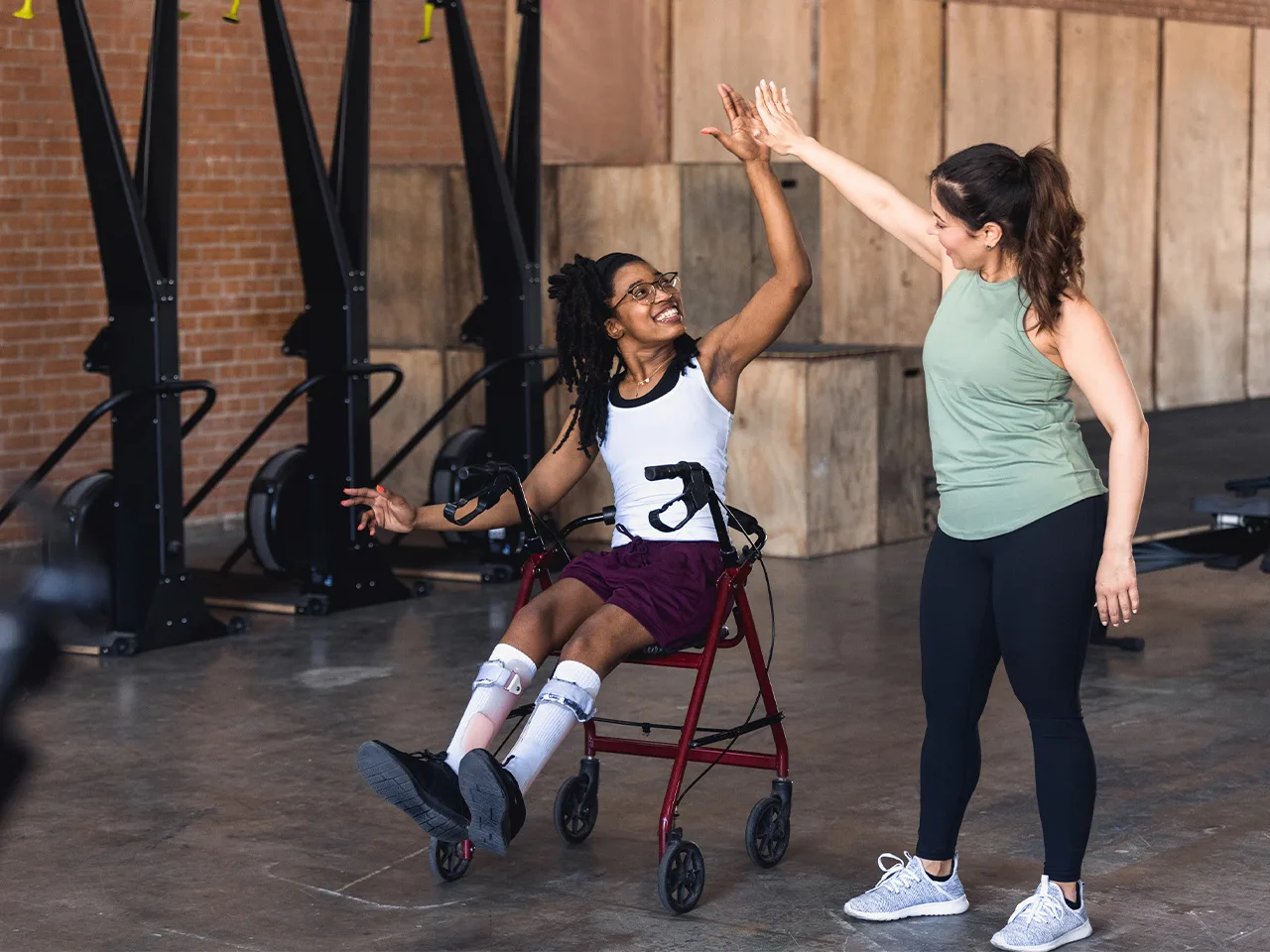 A woman using a mobility device high-fives a woman standing next to her.