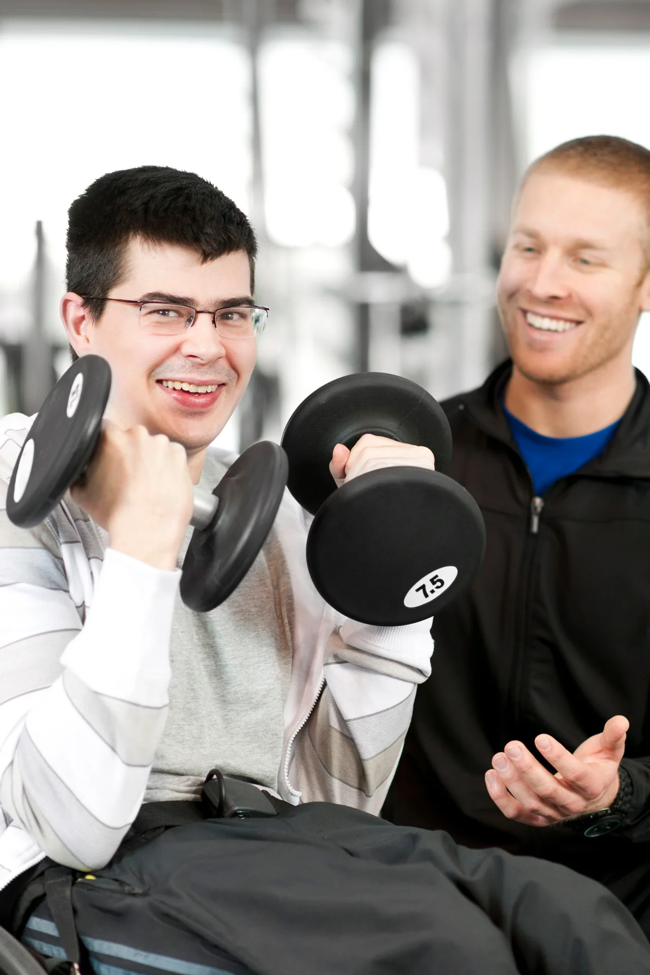 A man using a wheelchair exercises with a personal trainer using dumbbells.