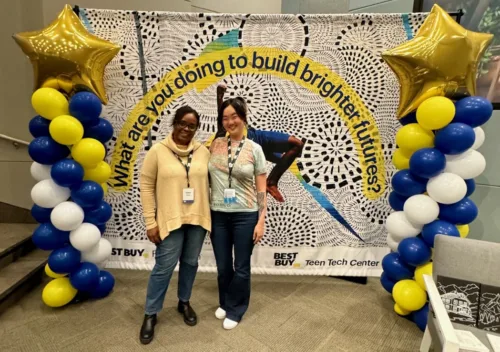 YMCA staff stand in front of a colorful banner announcing the Best Buy Teen Tech Center